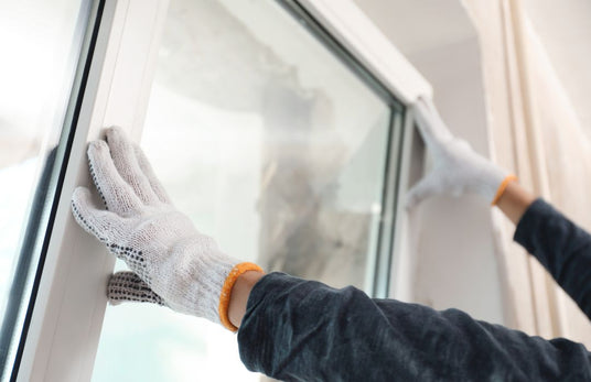 Handwerker baut ein Fenster ein mit Handschuhen an.
