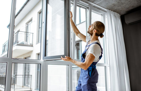 Ein Handwerker im Blaumann stellt den Flügel eines Fensters ein.